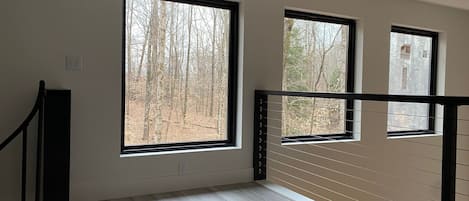 A room with large windows, a wooden floor, and a black railing.