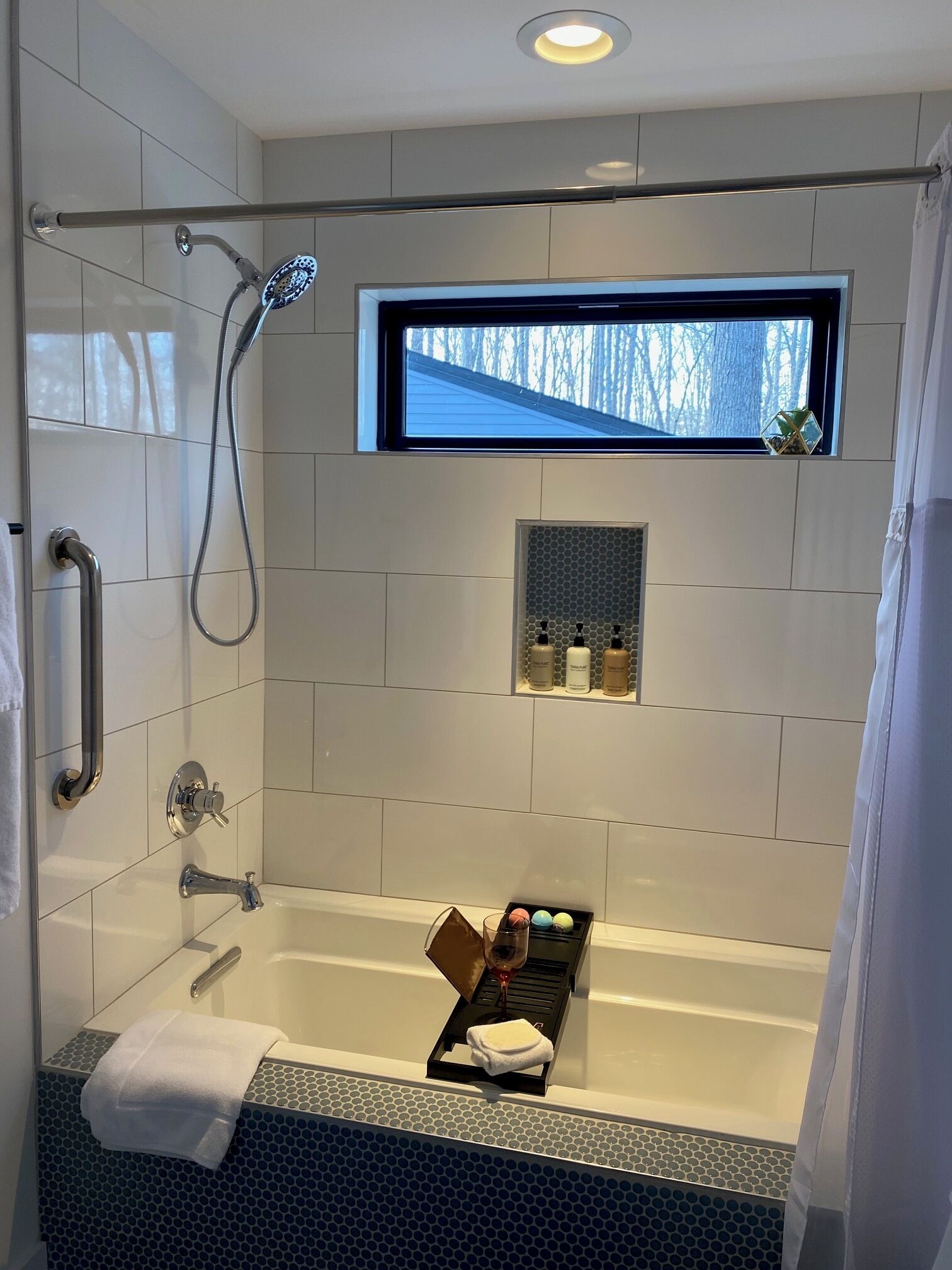 A modern bathroom with a glass shower enclosure, a built-in window, and a vanity with toiletries.