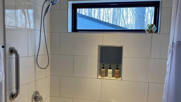 A modern bathroom with a glass shower enclosure, a built-in window, and a vanity with toiletries.
