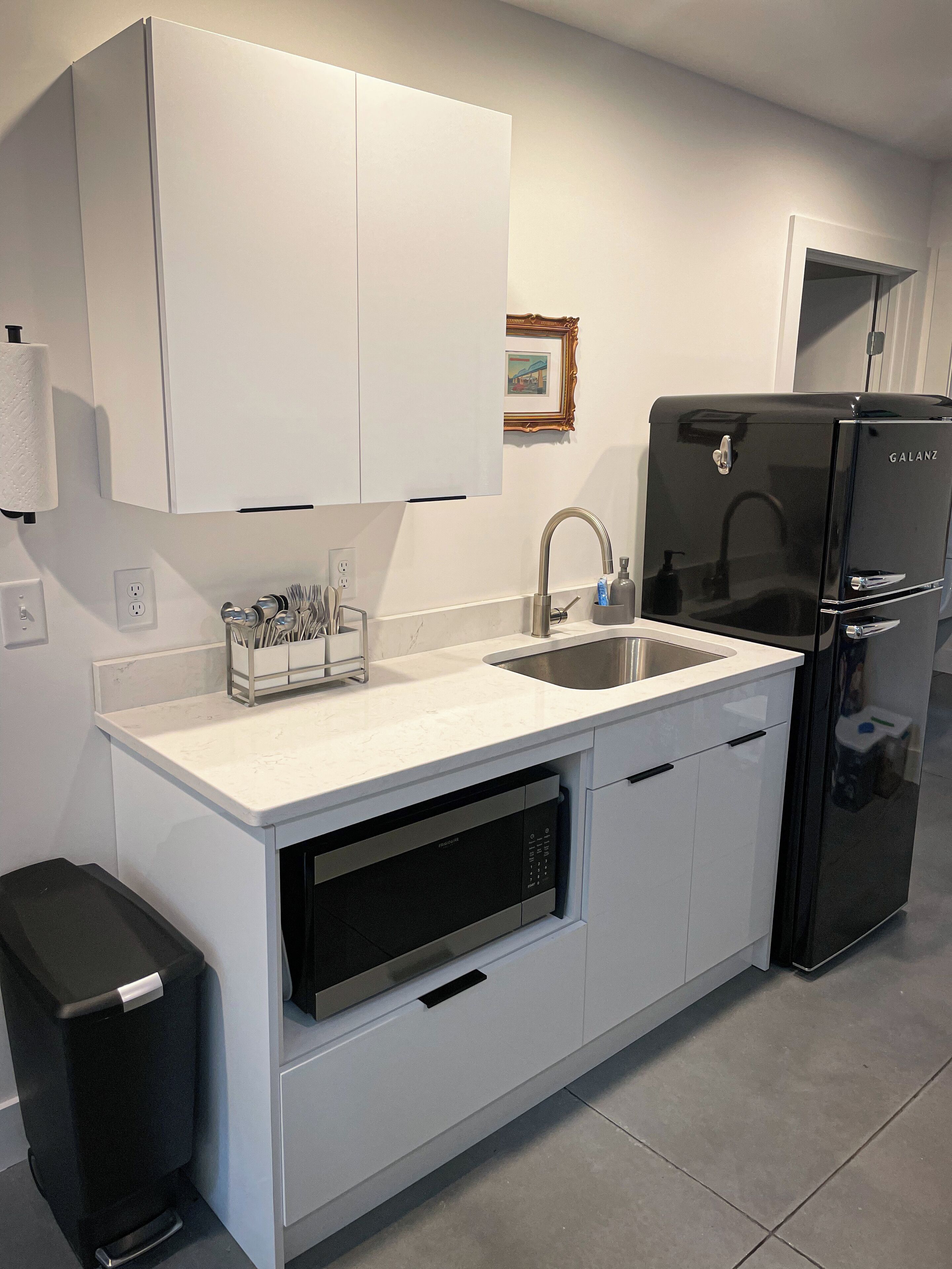 Una cocina moderna con armarios blancos, un lavamanos de acero inoxidable, un refrigerador negro y un lavavajillas.