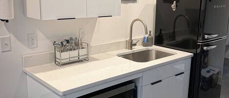 Una cocina moderna con armarios blancos, un lavamanos de acero inoxidable, un refrigerador negro y un lavavajillas.