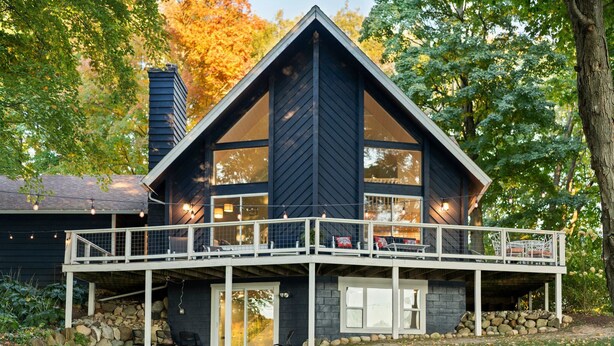 A modern cabin with a large deck, stone foundation, and large windows. - Lakefront Spacious Cottage with Sandy Beach, Kayaks and Games! (Gaylord)