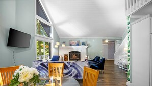 A spacious living room with a fireplace, a dining area with a glass table, and a TV mounted on the wall. - Lakefront Spacious Cottage with Sandy Beach, Kayaks and Games! (Gaylord)