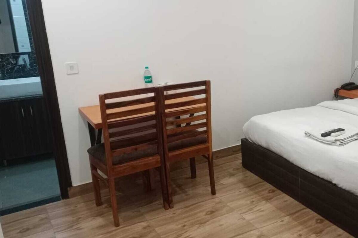 A hotel room with a wooden desk, a bed with white bedding, and a nightstand with a lamp and phone.