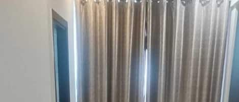 A room with a wooden parquet floor, a bed, a chair, and a curtain.