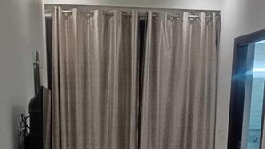 Une pièce dotée d’un plancher en bois, d’un rideau, d’un téléviseur à écran plat posé sur un meuble en bois, et d’une porte en verre donnant sur une autre pièce.