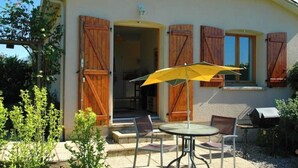 A building with wooden shutters, a patio with a table and chairs, and a barbecue grill. - Rural gite in the beautiful Lot et Garonne with air con. Heated swimming pool. (Coulx)