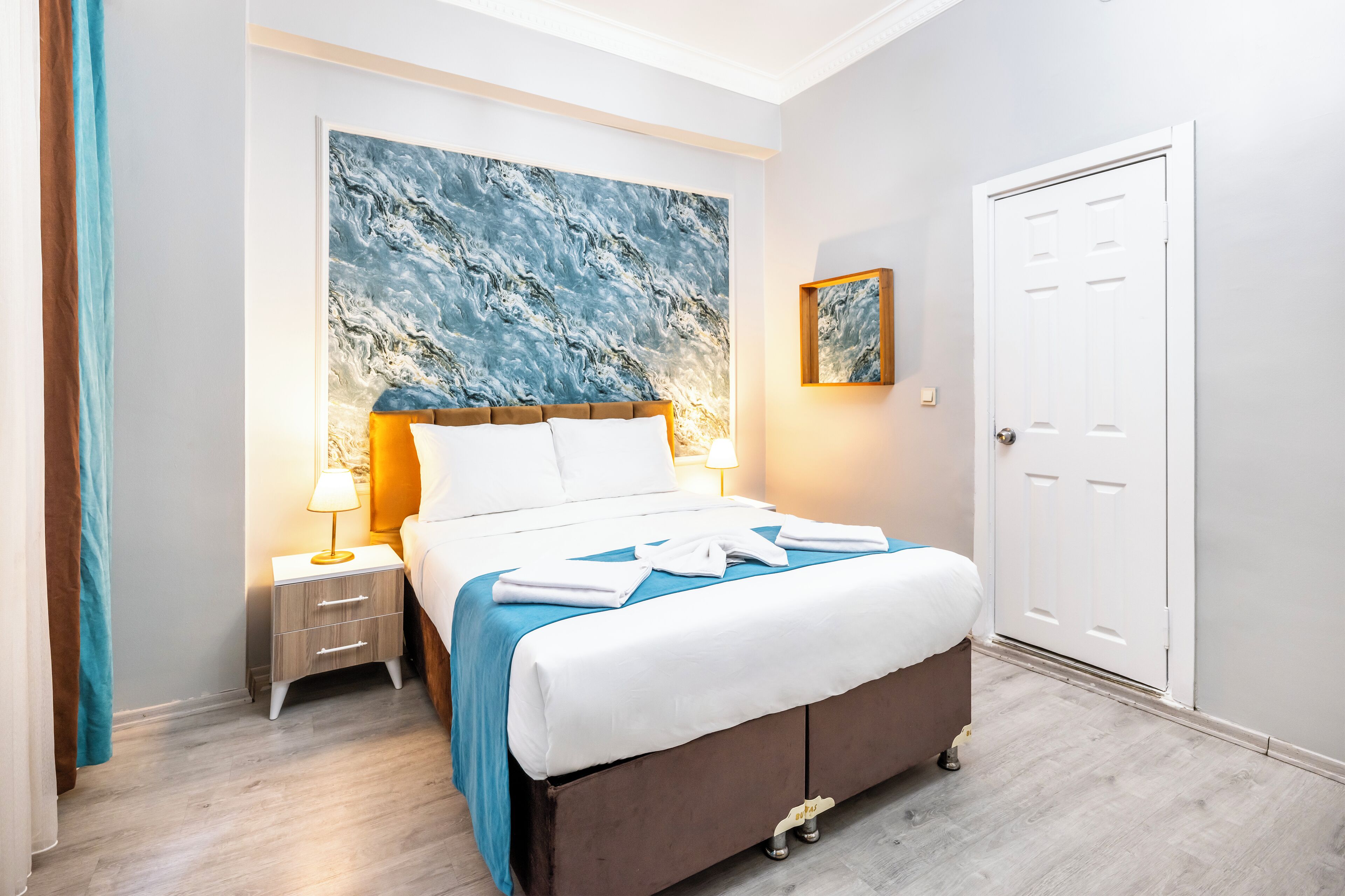 Una habitación de hotel con una cama, una mesita de noche, un cuadro y una puerta.