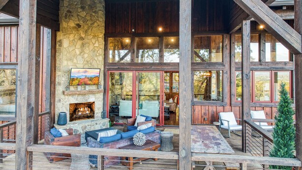 Una cabaña rústica con chimenea de piedra, terraza de madera y ventanas amplias.