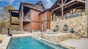 Una cabaña de madera con fachada de piedra, piscina y mobiliario de exterior.