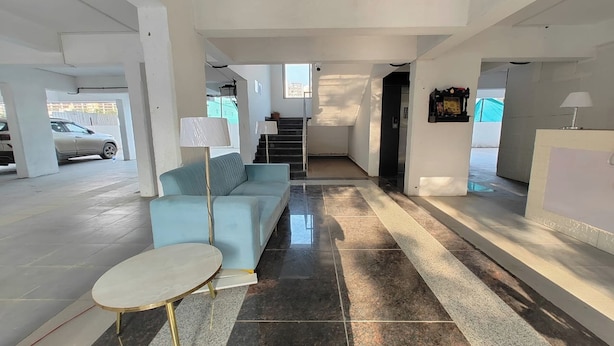 A spacious lobby with a light blue sofa, a small round table, and a staircase leading to an upper level. - Aanand Riddhi (Pune)