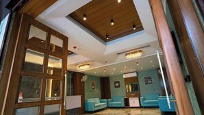 A spacious room with a high ceiling, wooden paneling, and a chandelier. There are two blue sofas and a small cabinet. - Hotel U Connect Near RTO Office, Udaipur (Udaipur)