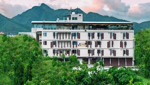 A multi-story hotel with a modern design, featuring balconies on each floor and a view of mountains in the background. - Hotel U Connect Near RTO Office, Udaipur (Udaipur)