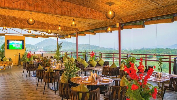 An outdoor restaurant with tables and chairs, a thatched roof, and a view of the mountains. - Hotel U Connect Near RTO Office, Udaipur (Udaipur)