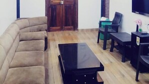 A living room with a sofa, a coffee table, a TV, and a wooden door. - Saubhagya Villa (Mahabaleshwar)
