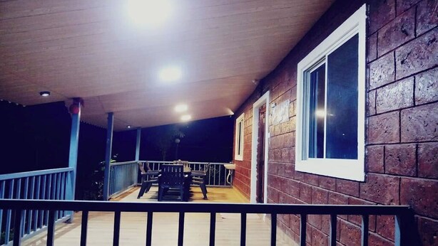 A covered outdoor area with a wooden deck, a railing, and a window. - Saubhagya Villa (Mahabaleshwar)