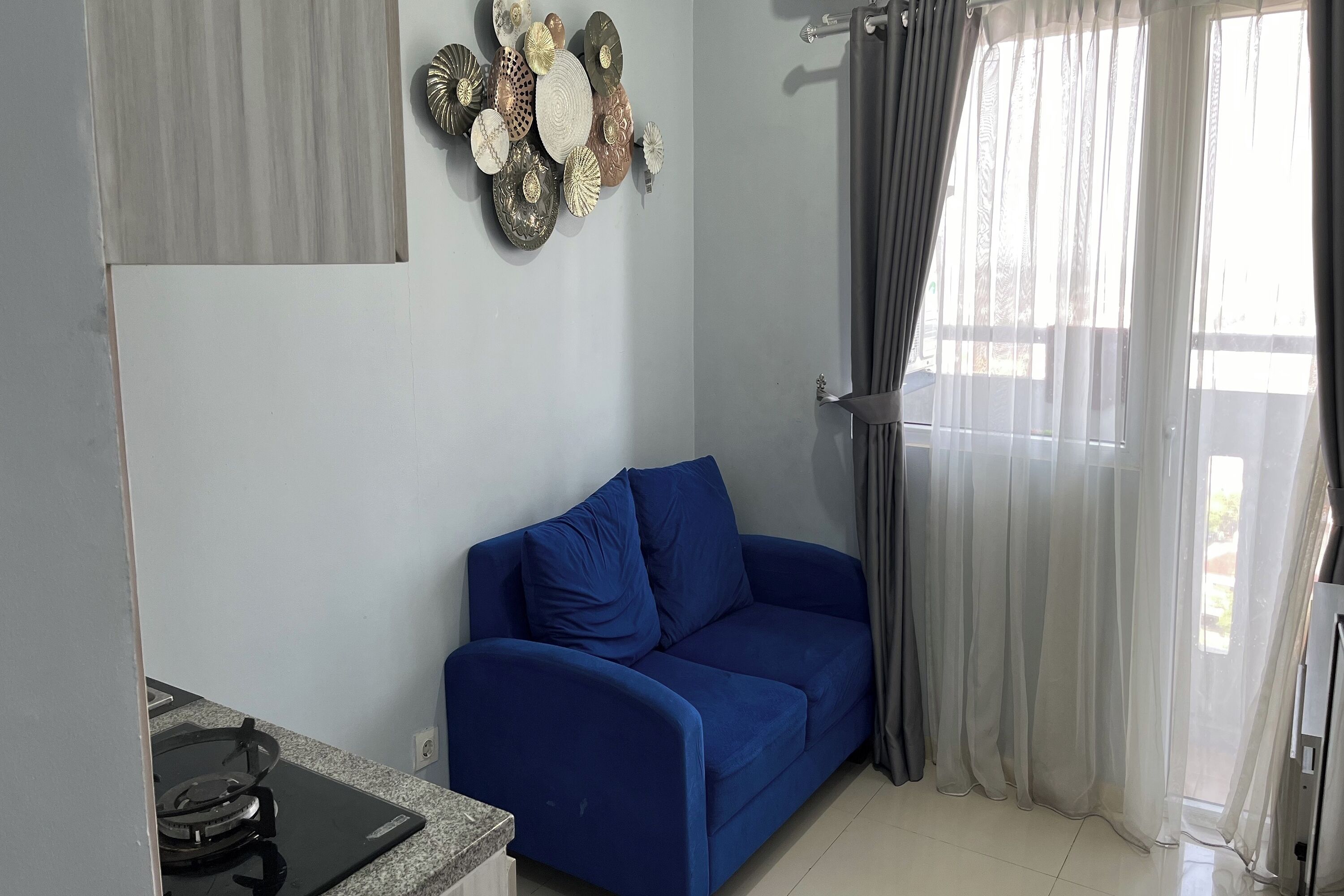 A living room with a blue sofa, a decorative wall piece, and a window with sheer curtains.