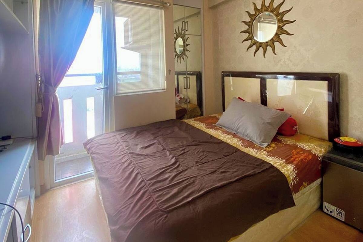A bedroom with a bed, a nightstand, a mirror, and a window with curtains.