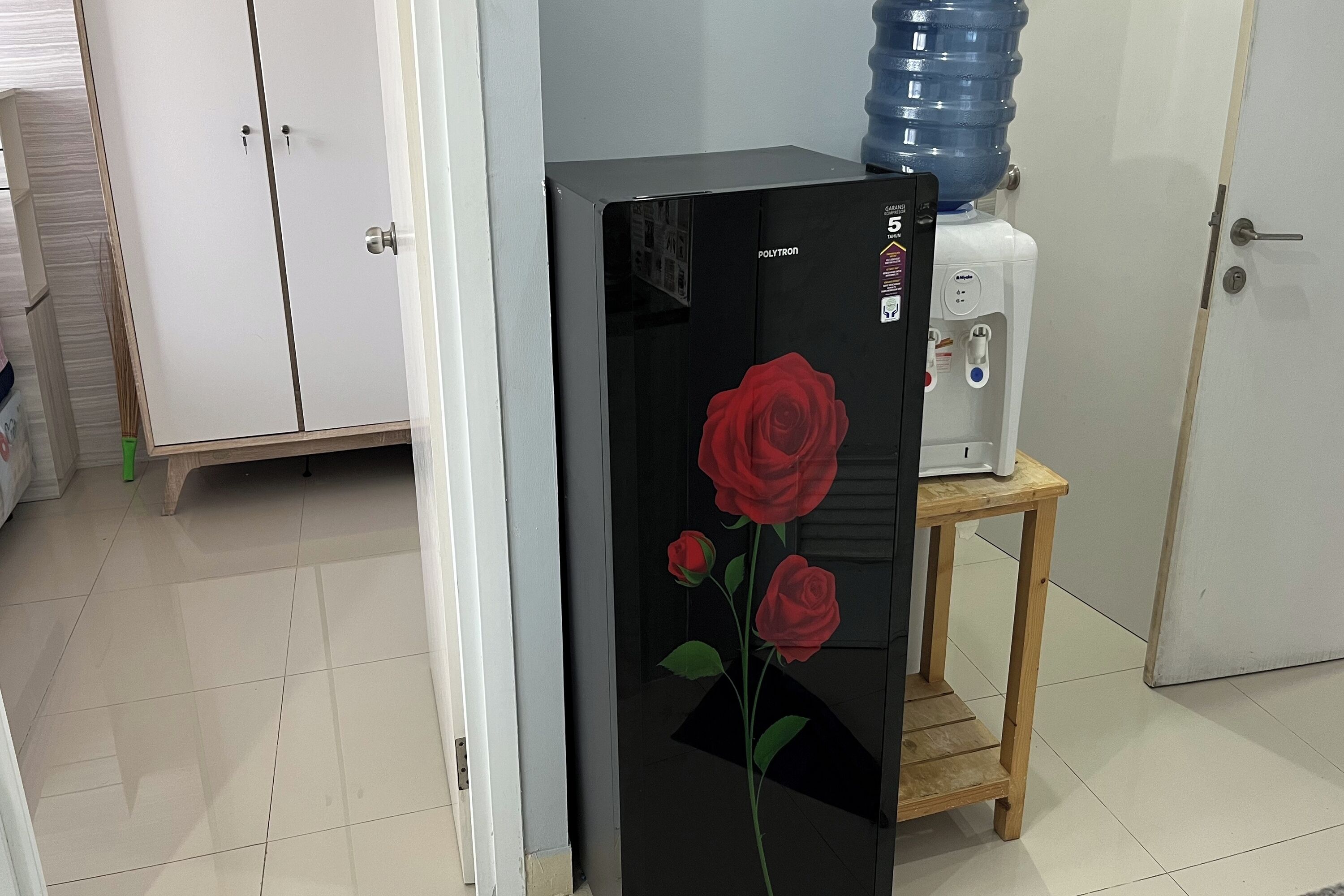 Habitación con refrigerador decorado con un diseño de rosa, dispensador de agua y una pequeña mesa de madera.