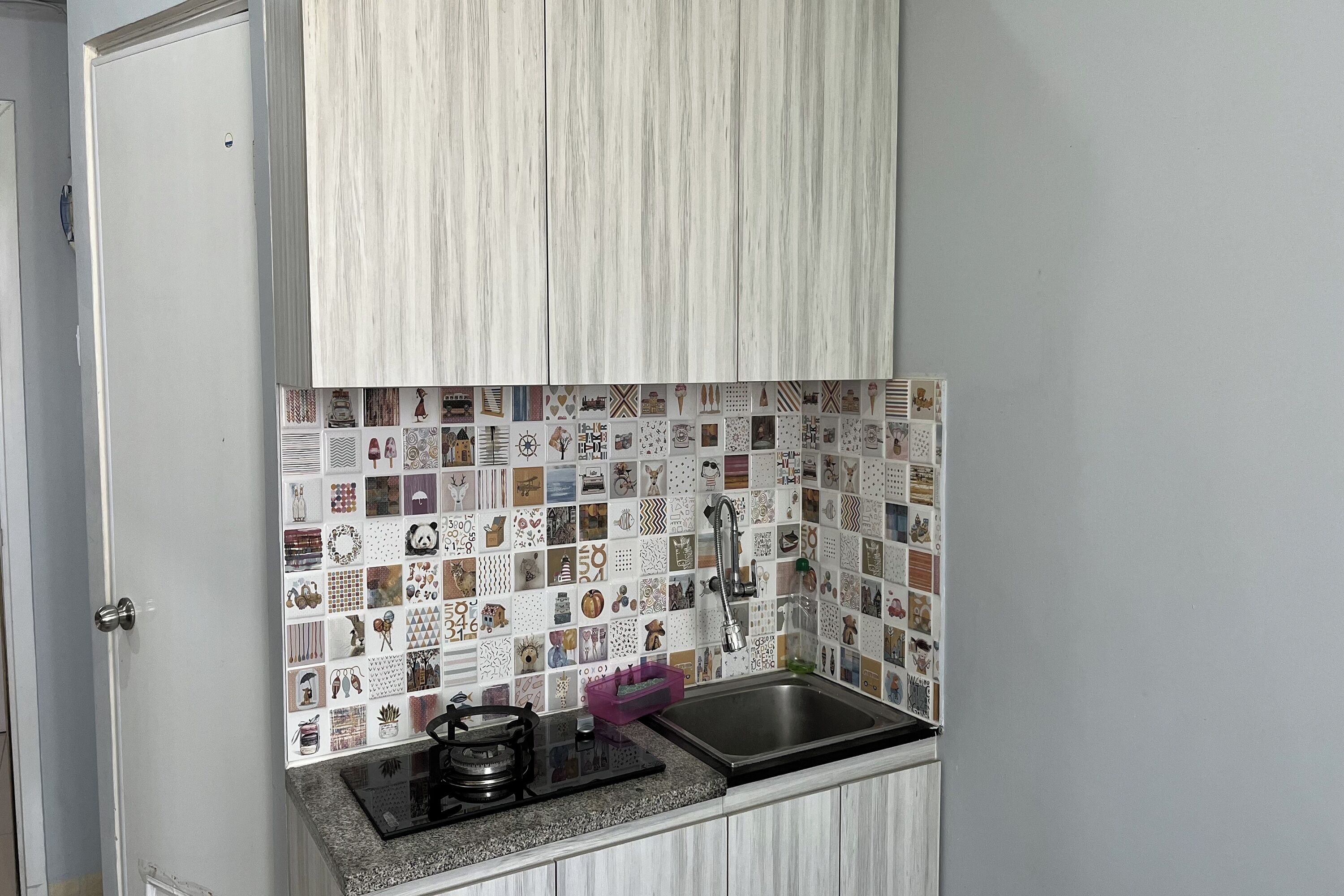 Una cocina con salpicadero de azulejos, un lavabo de acero inoxidable y una estufa a gas.