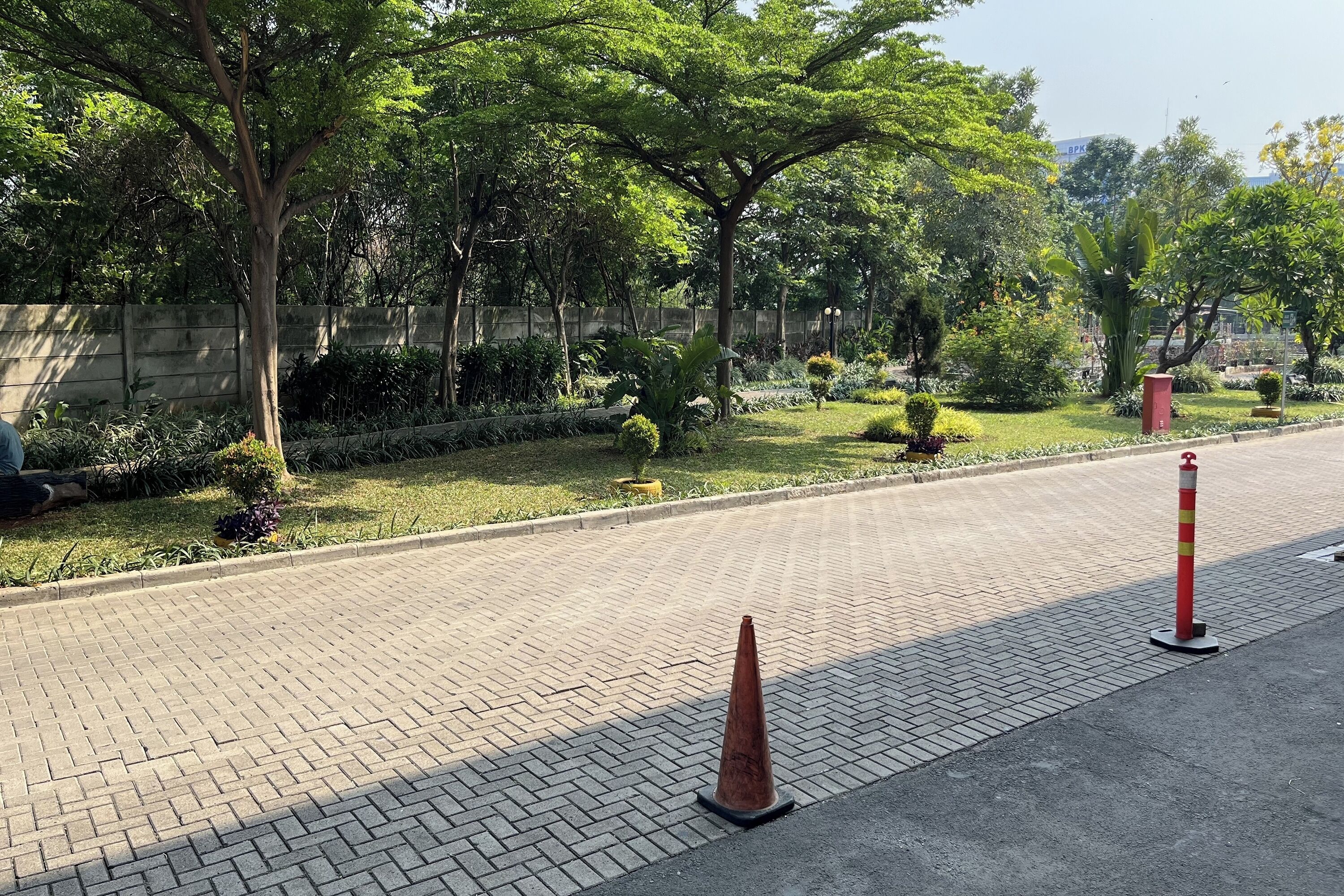 A paved pathway with a brick pattern, surrounded by lush greenery and trees.