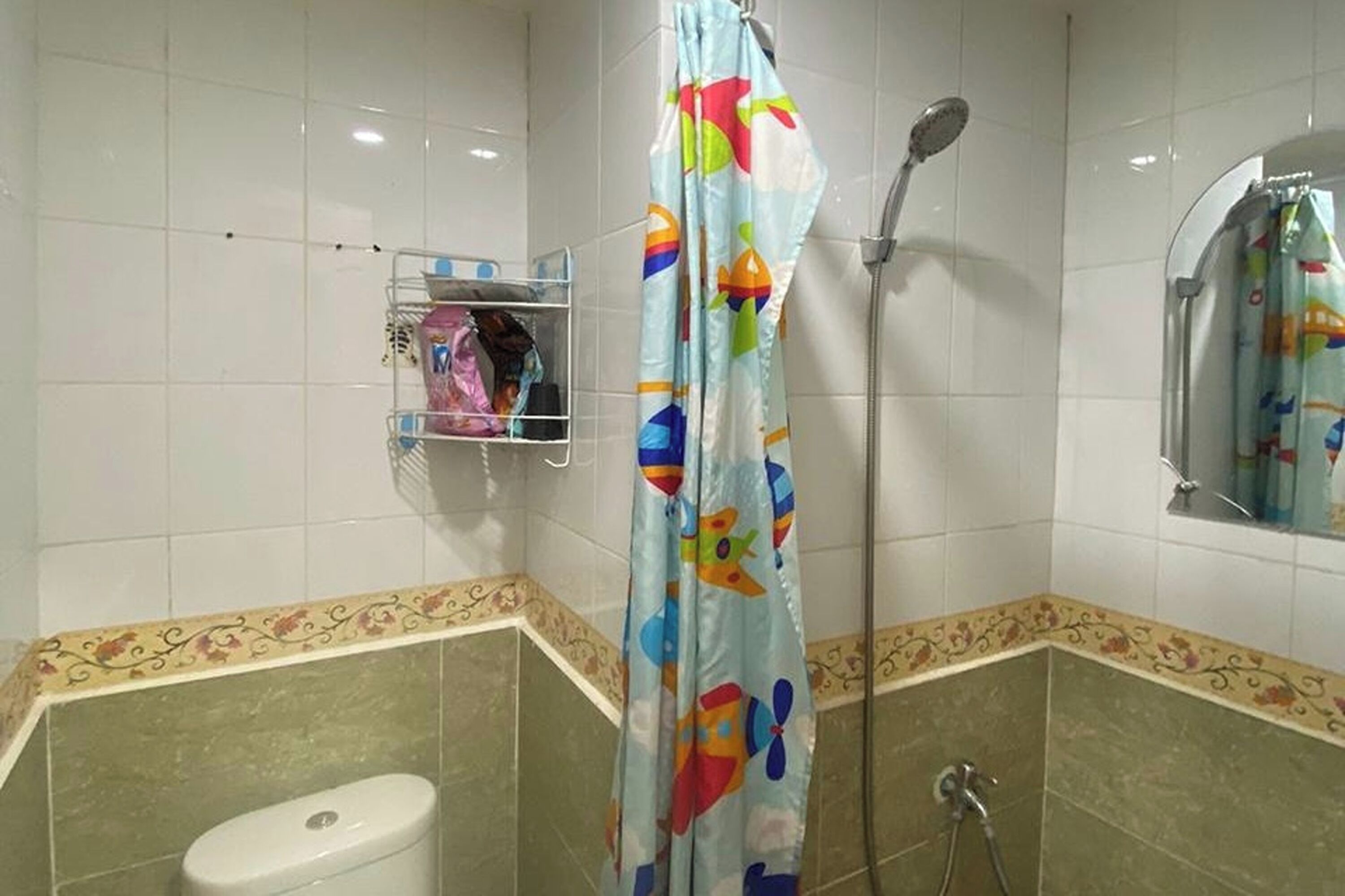 Een badkamer met douchegordijn met kleurrijke vismotieven, een toilet en een plank met toiletartikelen.