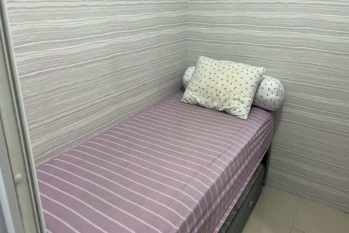 A small, single-bed room with a striped bedspread and two pillows.