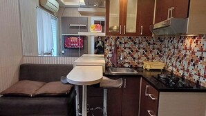 A compact kitchen with a dining area, a built-in oven, and a tiled backsplash. - Green Pramuka By Uchi Property (Jakarta)