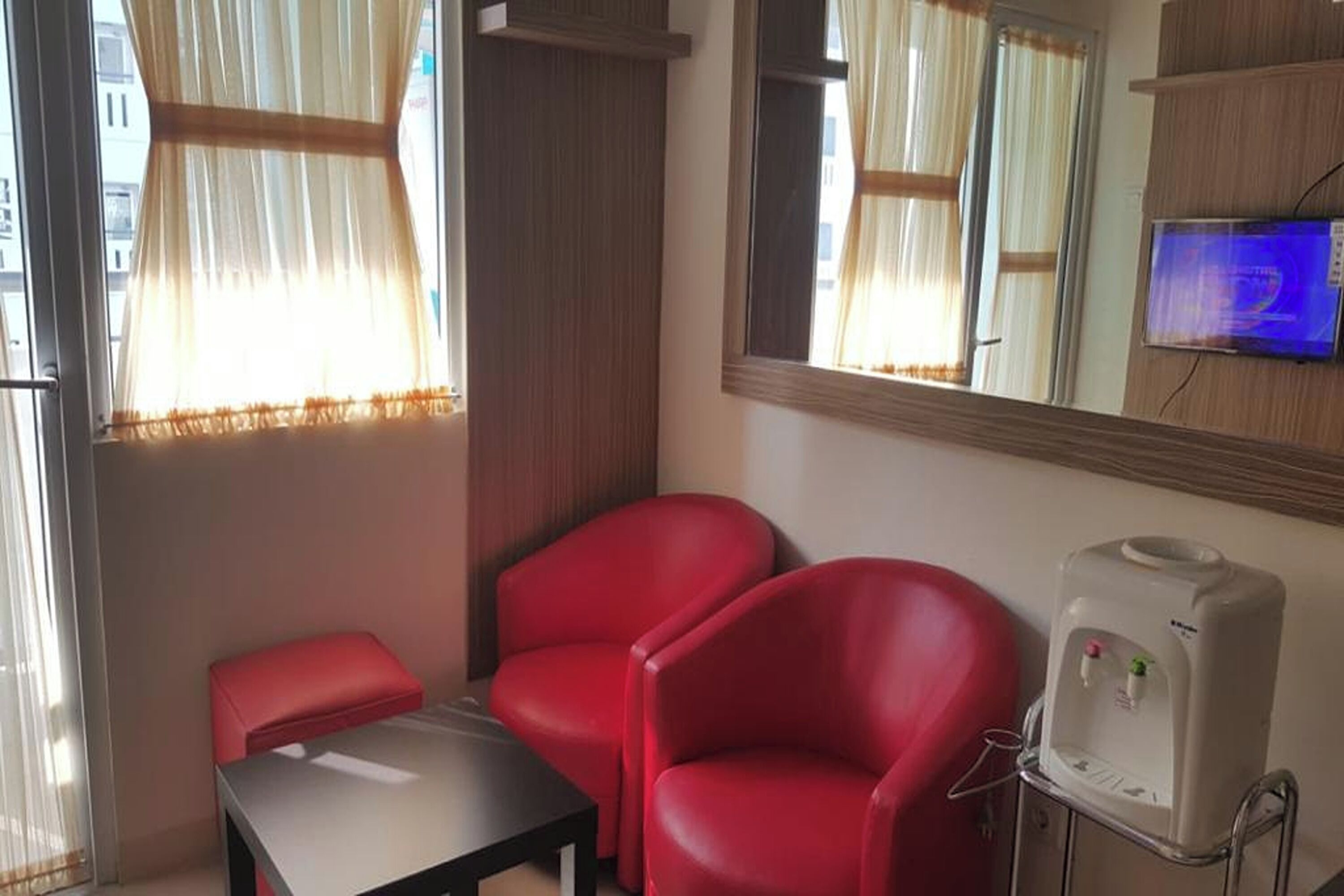 A room with a red chair, a small table, a water dispenser, and a TV on the wall.