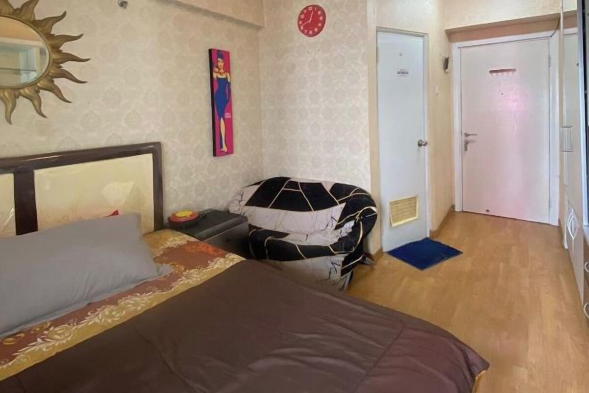 A hotel room with a bed, a nightstand, a clock, and a door.