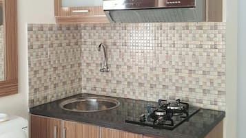 Una cocina con salpicadero de azulejos, un lavamanos de acero inoxidable, armarios de madera y una encimera negra con una estufa.