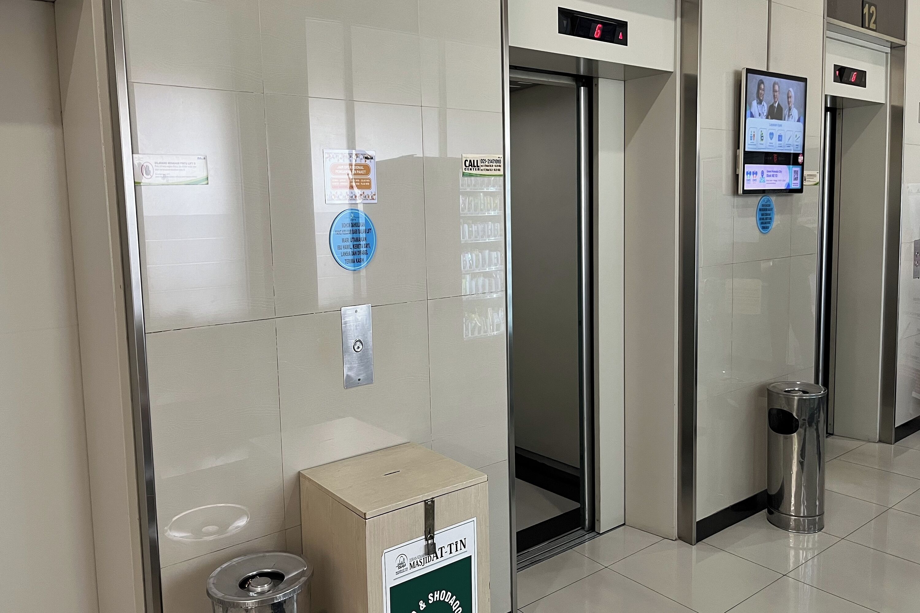 An elevator interior with digital displays, a trash bin, and informational signs.