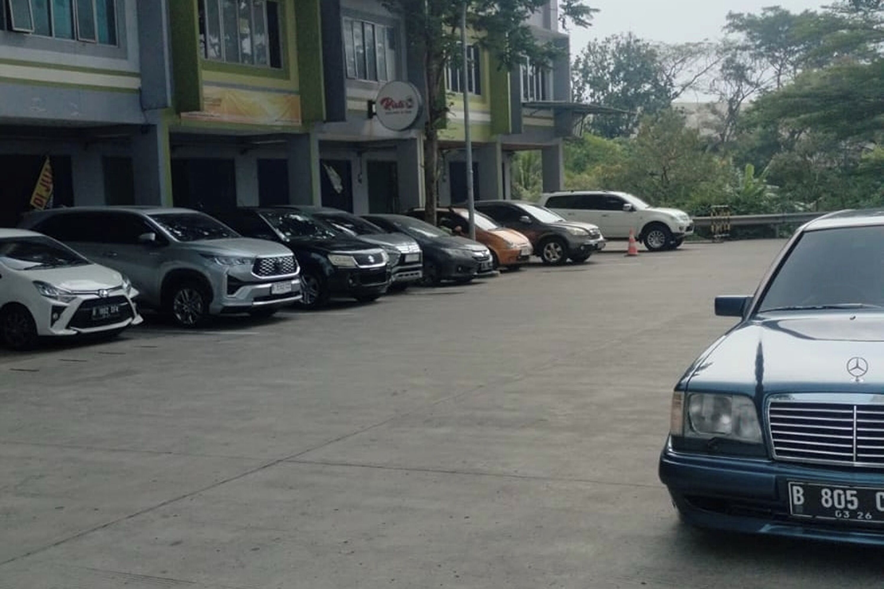 A parking lot with several parked cars, including a Mercedes-Benz, in front of a building with a sign that reads "Punto."