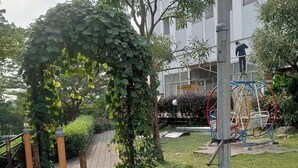 Egy park, amelyben mászófal található, egy kiépített sétaút vezet végig, és a háttérben egy épület látható.