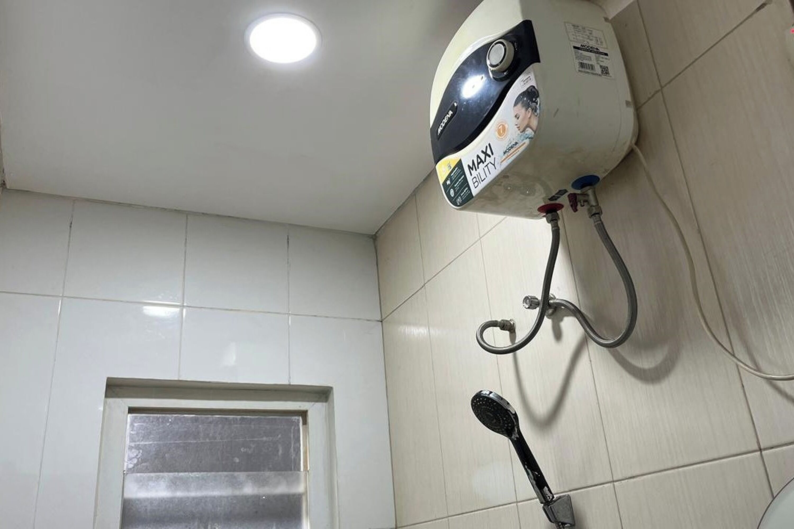 A bathroom with white tiled walls, a shower with a handheld showerhead, and a ceiling-mounted water heater.