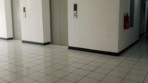 Egy folyosó, csempézett padlóval, ajtókkal és egy lift vezérlőpaneljével.