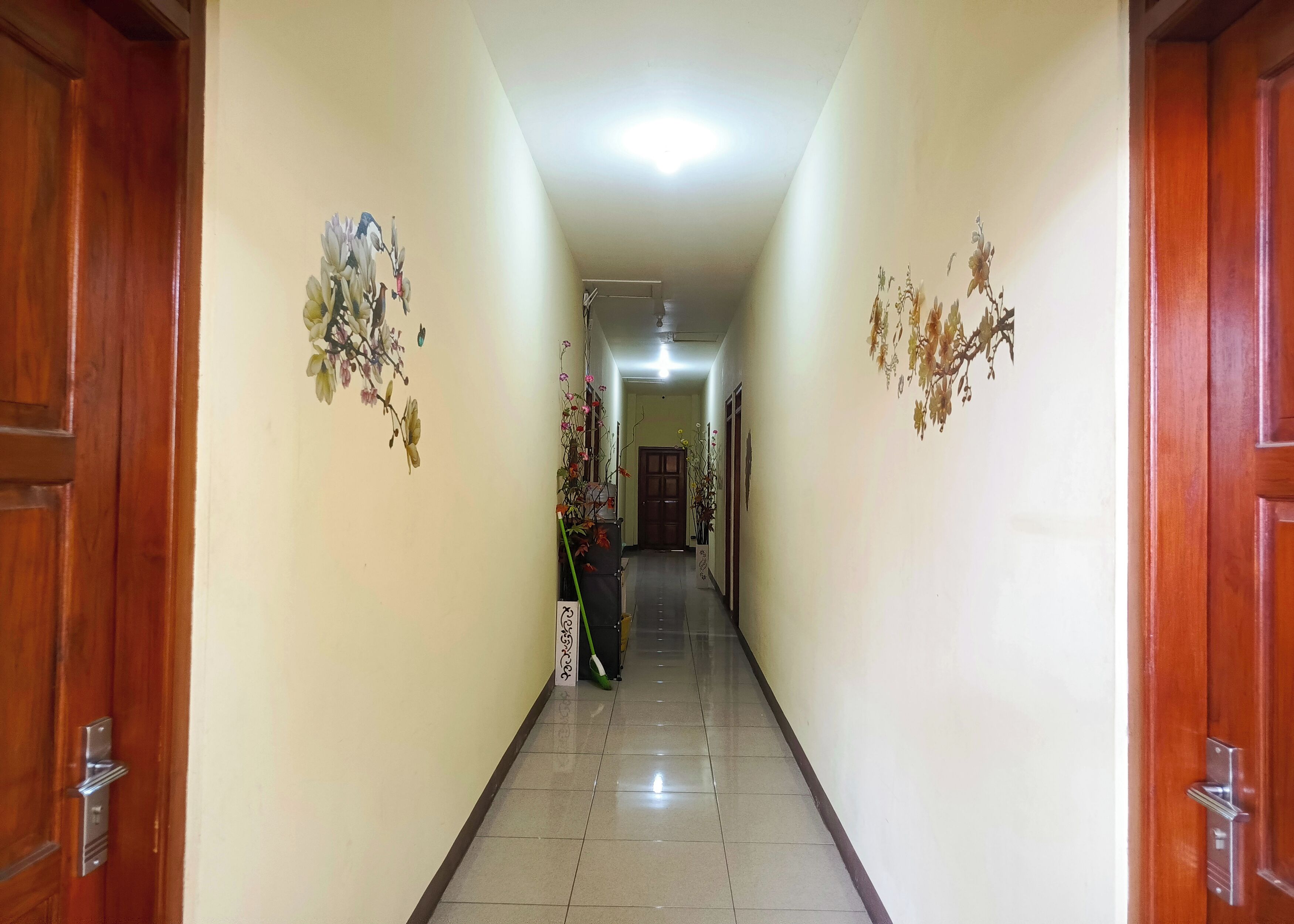A hallway with wooden doors on either side, tiled floor, and floral wall decorations.