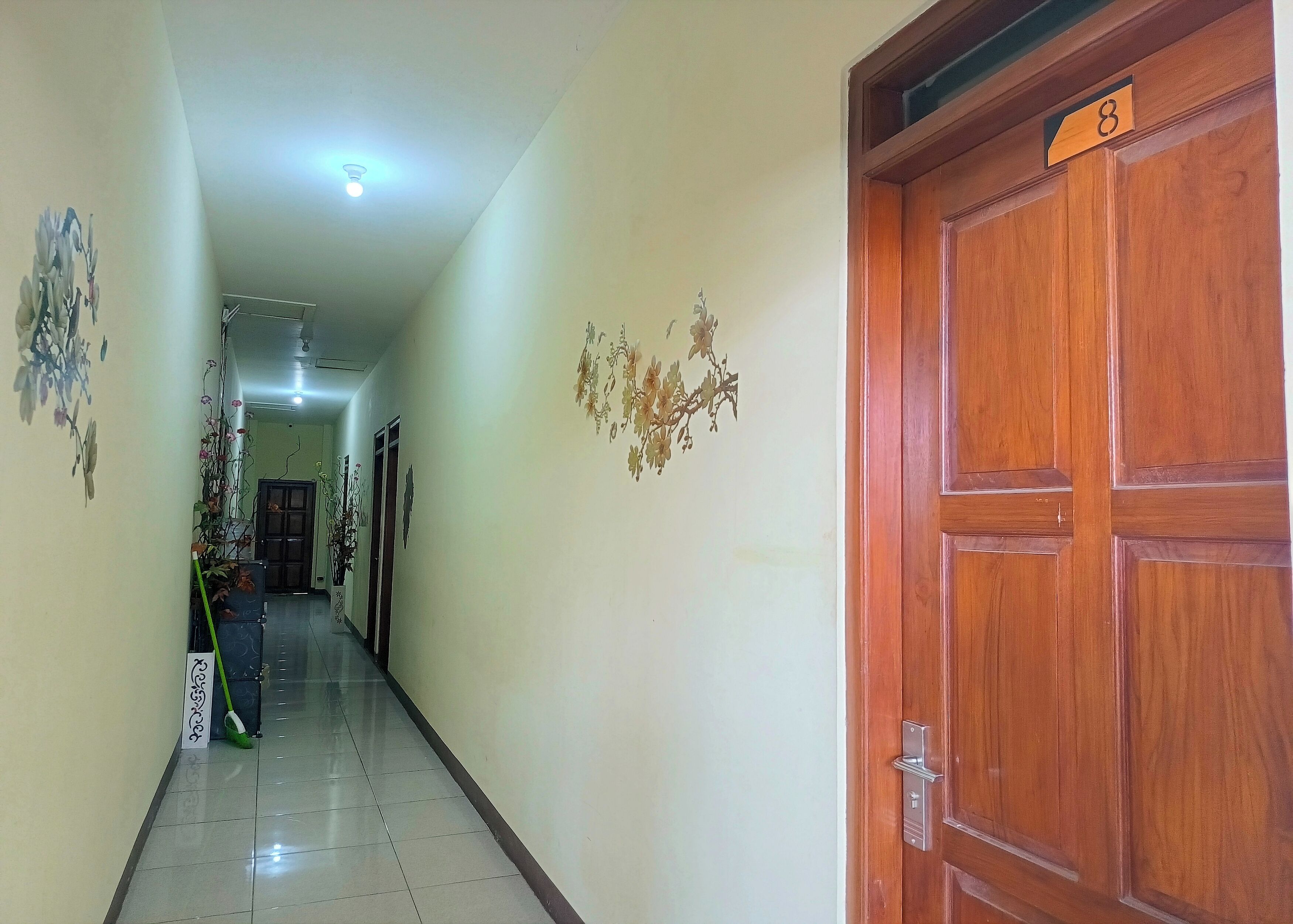 A hallway with a wooden door marked with the number 8, a tiled floor, and wall-mounted floral decorations.