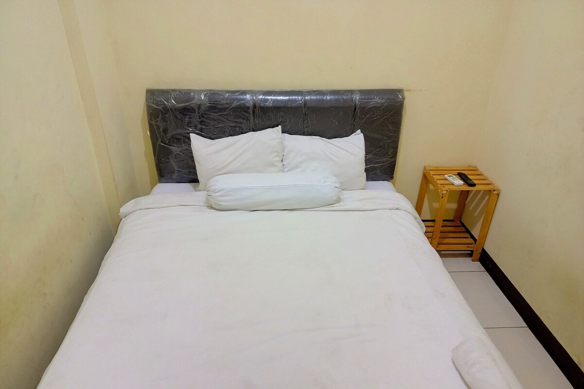 A neatly made bed with white linens and pillows, a wooden nightstand with a remote control, and a marble-patterned headboard.