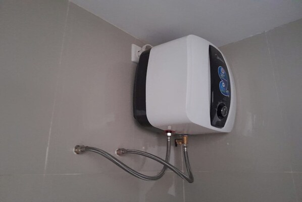 A water heater mounted on a tiled wall with two visible hoses connected to it.