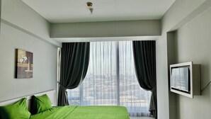 A modern hotel room with a large bed, a view of the city through sheer curtains, and a mounted television.