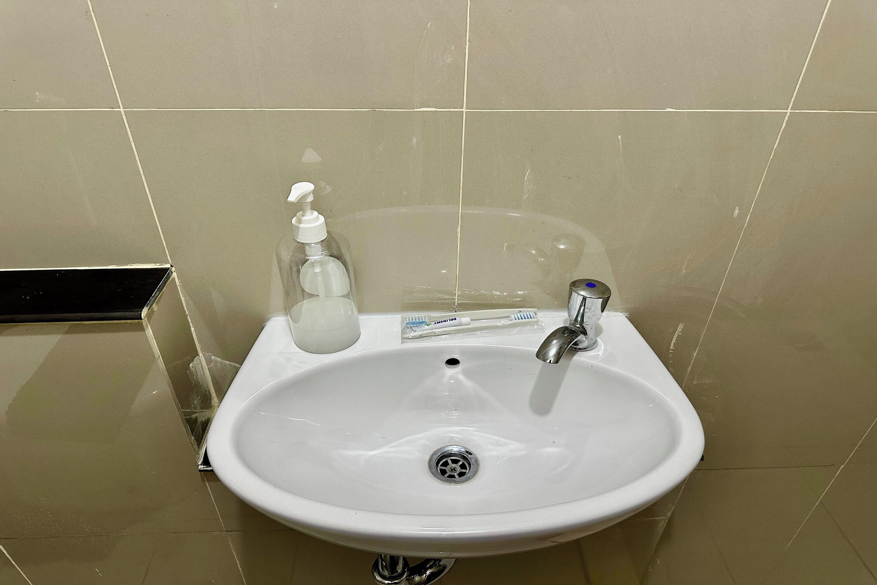 Un lavamanos blanco con grifo cromado, dispensador de jabón y porta cepillos de dientes.