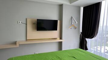 Una habitación de hotel con una cama, un televisor montado, una ventana con cortinas y un estante de madera.