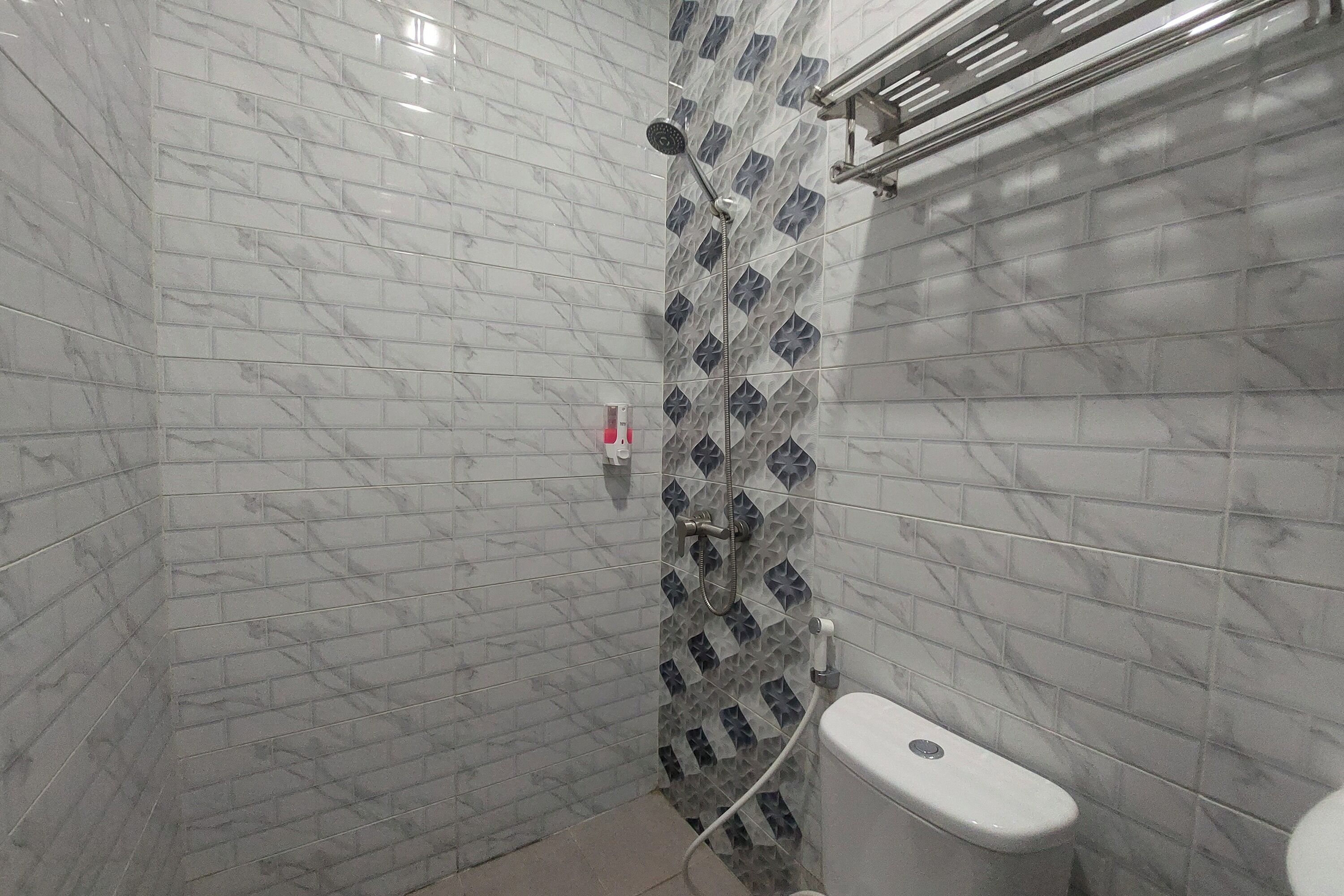 Une salle de bain carrelée de marbre, une douche avec un pommeau de douche à pluie et des toilettes.