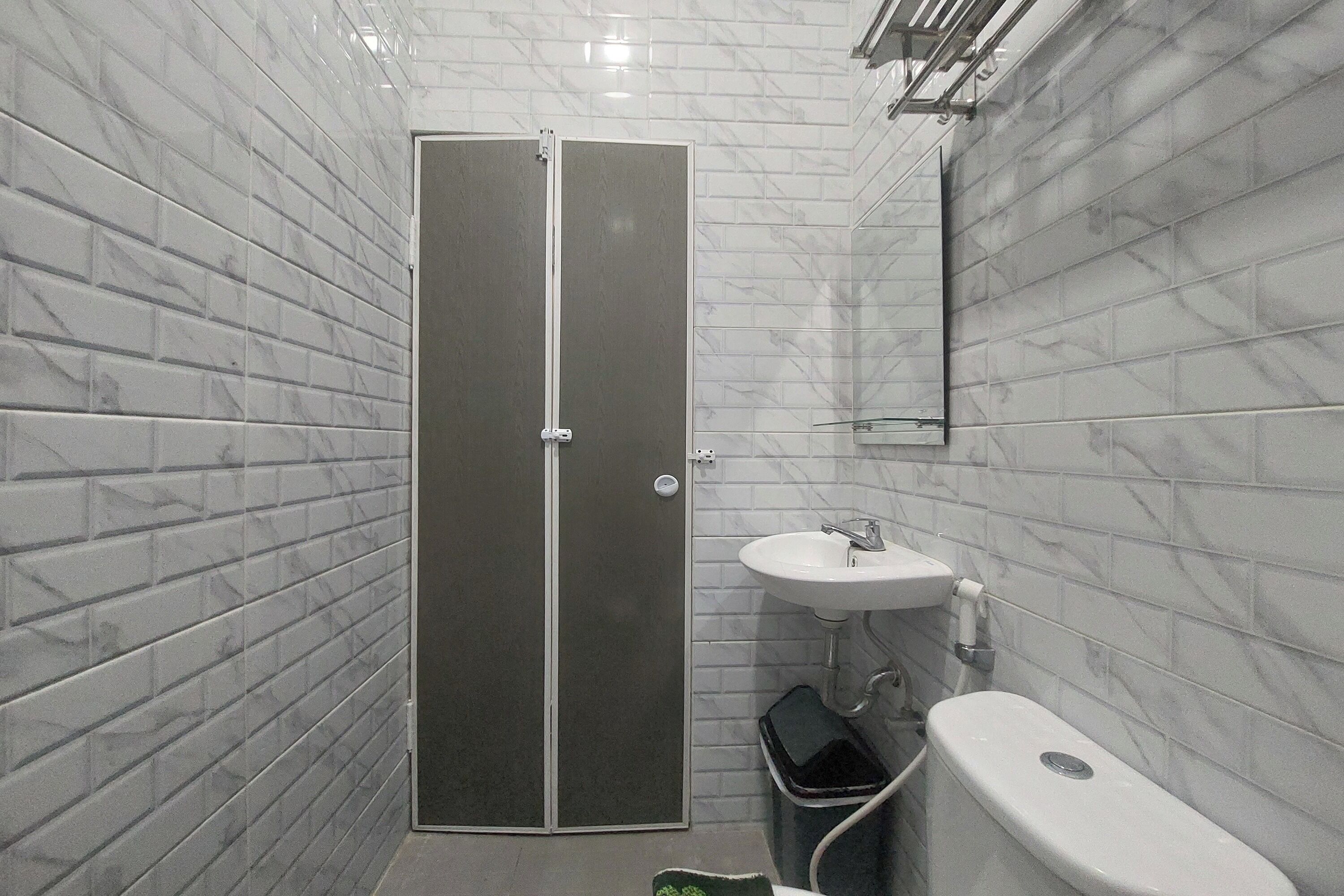 Un baño con azulejos de mármol blanco, puertas dobles, un lavabo y un inodoro.