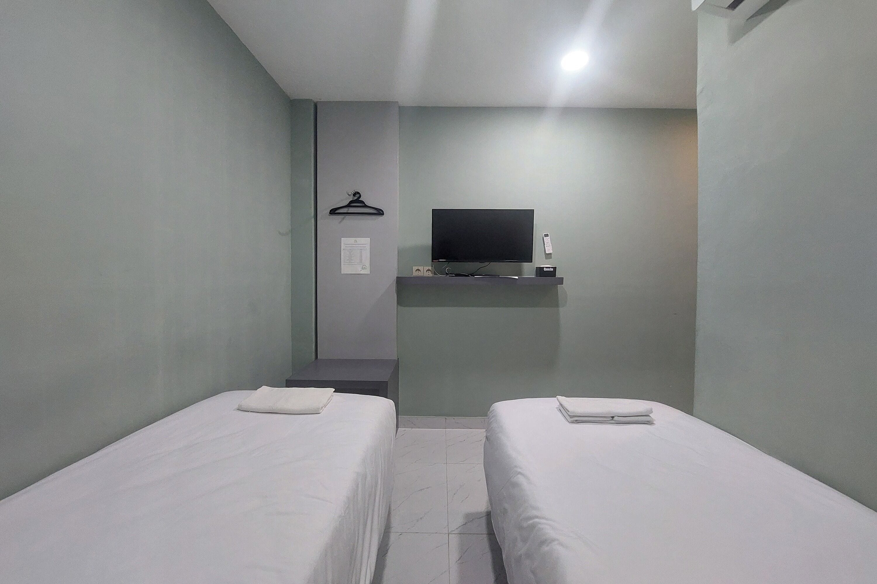 A small, clean room with two single beds, a flat-screen TV mounted on the wall, and a small table with a remote control.