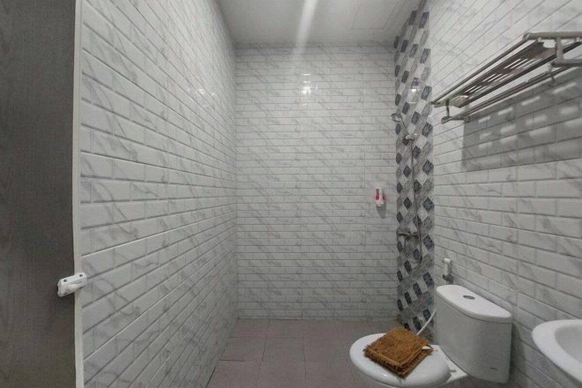 A small, narrow bathroom with white marble tiles, a toilet, a sink, and a towel rack.