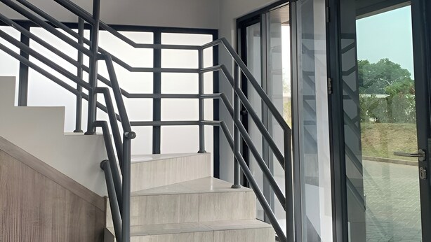 A staircase with a modern design, featuring a metal railing and glass doors leading to an outdoor area. - Riverdale Cikarang By Veto Rooms (Cikarang)