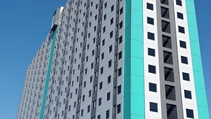 A high-rise building with a modern architectural design, featuring a grid of windows and a prominent vertical structural element. - Riverdale Cikarang By Veto Rooms (Cikarang)