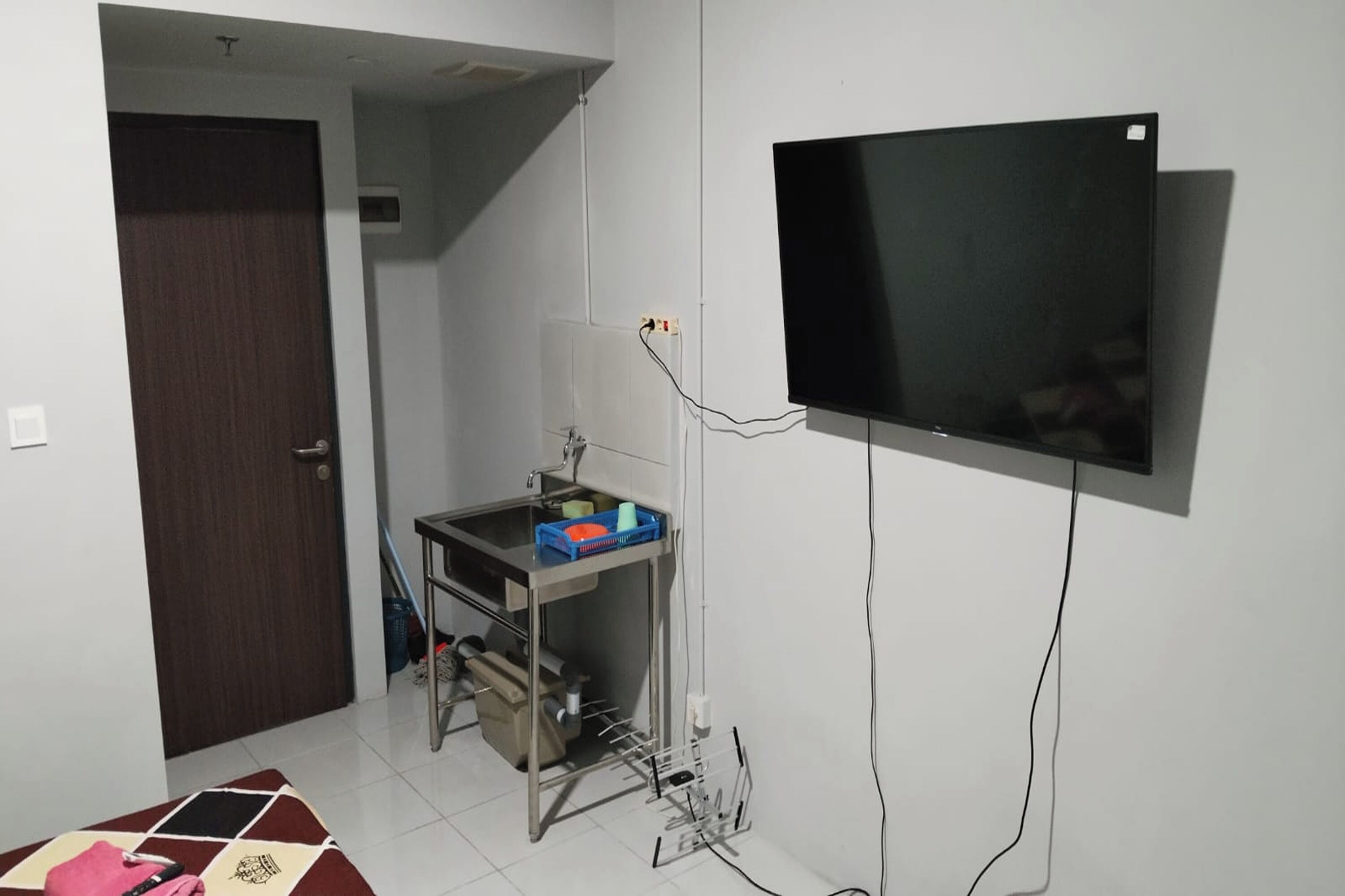 A small room with a TV mounted on the wall, a desk with a computer, and a door leading to another room.